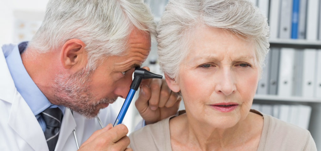 Close-up of a male doctor examining senior patient's ear at the medical office